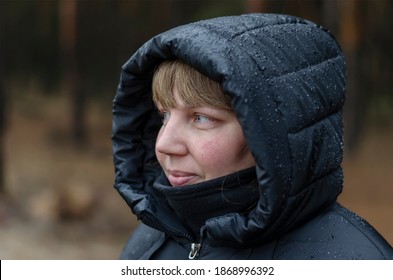 Portrait Of A Middle-aged Woman In Black Hooded Jacket In  Autumn Rain. Woman Of 40-45 Years Old Looks Carefreely Past The Camera. Lifestyle.