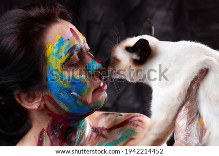 Portrait of middle-aged woman with unusual makeup and siames cat. Painting smears, abstract makeup. Vivid paint make-up, bright colors
