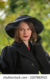 Portrait Of Middle-aged Woman Wears Black Coat Hat With Veil And Looks Mysteriously To Side. Woman From High Society Aristocrat Outside