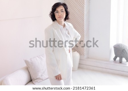 Portrait of a middle-aged woman in a white business suit. Against the backdrop of a bright modern interior.