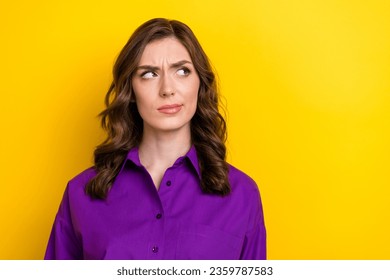 Portrait of minded puzzled girl with curly hairdo wear violet blouse thoughtfully look at empty space isolated on yellow background