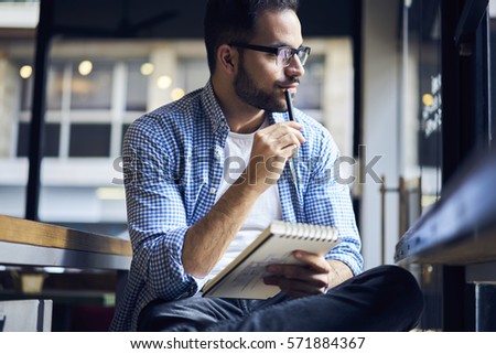 Portrait of mindful male designer dressed in casual clothes working during vacations searching for inspiration looking out the window while creating graphic outlay for apartment interior in notebook