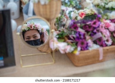 Portrait In The Mirror Of A Woman Wearing A Black Mask And Wearing A Flower Crown. Blurred Background.