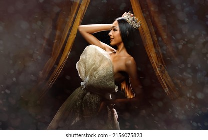 Portrait Of Miss Beauty Pageant Contest Woman With Sparkle Diamond Crown With Tanned Skin Beautiful Makeup Evening Gown On Stage With Lighting Curtain And Dark Background