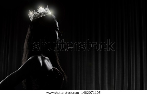 Portrait of Miss Pageant Beauty Contest in\
sequin Evening Ball Gown long dress with sparkle light Diamond\
Crown, silhouette low key exposure with curtain, studio lighting\
dark background\
dramatic