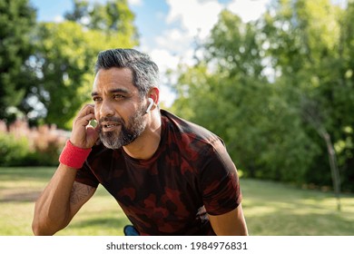 Portrait of mixed race sports man resting after run at park with copy space while listening to music. Middle adult indian jogger adjusting wireless earphone while running outdoor. Active mature man. - Powered by Shutterstock