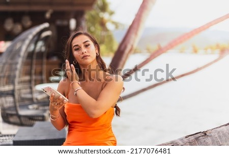 Portrait of mixed race woman in orange dress holding cell phone.