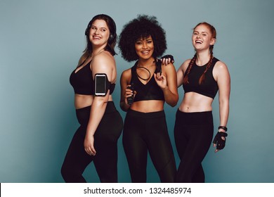 Portrait of mixed race women standing together against grey background and laughing. Diverse group women in sportswear.
