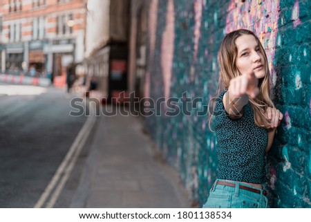 Portrait model pointing towards the camera wearing blue top and aqua jean shots in camden market area london near a graffiti wall