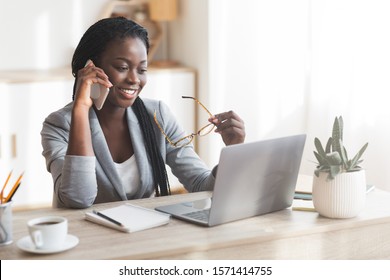 Portrait Of Modern Black Business Lady Talking On Cellphone And Working On Laptop In Office, Free Space