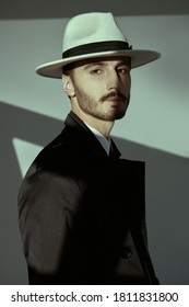 Portrait Of A Modern Businessman. Handsome Man In Elegant Black Suit, White Shirt And White Hat Posing On A Grey Background With Shadows. Men's Beauty, Fashion.