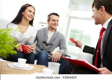 Portrait Of Modern Couple Looking At Real Estate Agent Giving His Visiting Card