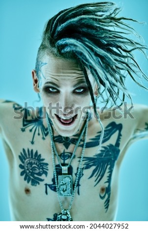 Portrait of a modern expressive punk rock musician looking at camera and shouting. Youth alternative culture. Studio portrait on a blue background. 
