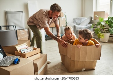 Portrait Of Modern Father Playing With Two Boys In Cardboard Box While Family Moving To New House, Copy Space