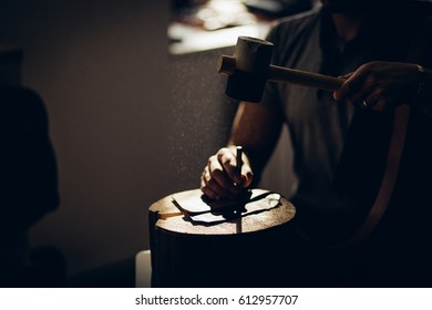 Portrait of modern handsome craftsman wearing creative cup focused on his work, taking measurements from rough leather in studio. focus on hammer