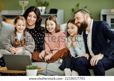 Portrait of modern jewish family using laptop and calling by video chat in cozy home setting