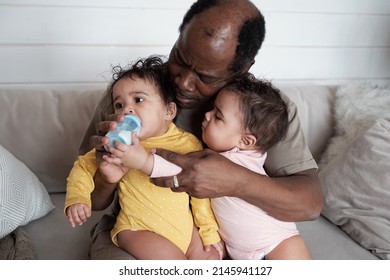 Portrait Of Modern Mature African American Father Taking Care Of His Twin Babies Bottle Feeding One Of Them