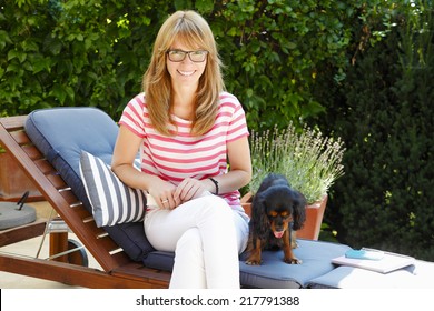 Portrait Of Modern Mature Woman Sitting At Garden With Her Puppy.