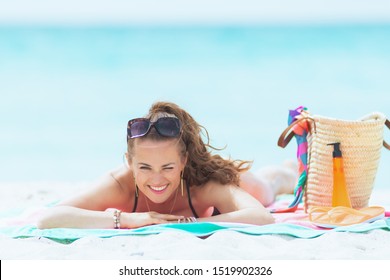 Portrait Of Modern Middle Age Woman With Long Curly Hair In Elegant Black Swimsuit On A White Beach Sun Bathing.