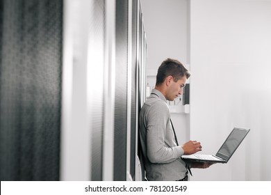 Portrait Of Modern Young Man Holding Laptop Standing In Server Room Working With Supercomputer