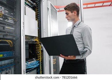 Portrait Of Modern Young Man Holding Laptop Standing In Server Room Working With Supercomputer