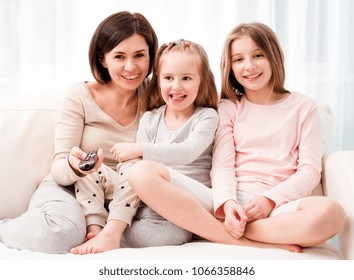 Portrait Of Mom Hugging Her Cute Daughters While Sitting On The Sofa And Watching TV At Home. Happy Family Relaxing On The Coach