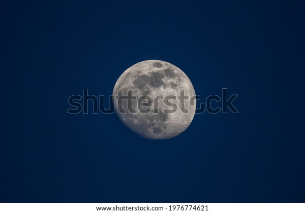 A\
portrait of the moon in a dark blue sky. The moon is in between a\
full and a half moon and is centered in the\
frame.