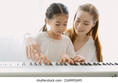 Portrait of mother Asian teaching her daughter playing a piano in living room at home. Spend time weekend together, happy mother and daughter. Creating activities to strengthen skills for children. - Powered by Shutterstock