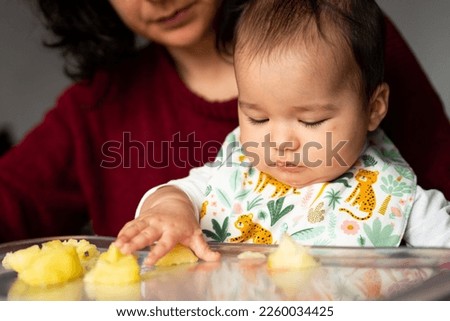 Portrait of mother and baby sitting at the table, and feeding her. close up. The concept of feeding and weaning baby from the breast. Hispanic family