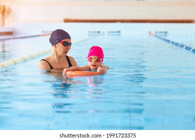 Portrait of mother or coach learning to swim with flutter board little girl at the public swimming-pool. Space for text - Powered by Shutterstock