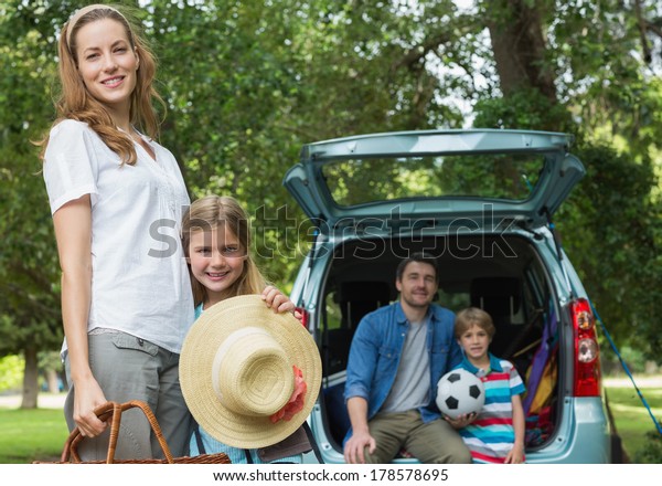 Portrait of mother and daughter with father and son\
sitting in car trunk