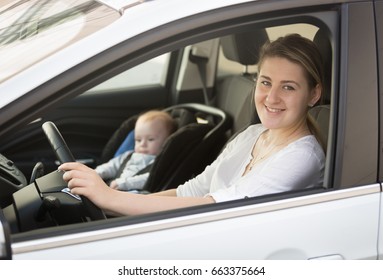 Portrait Of Mother Driving Car With Little Baby Boy Sitting In Safety Seat