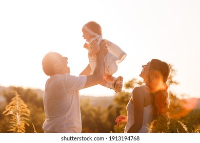 Portrait Of A Mother, Father Holds, Throws Up And Spins The Daughter On Hands Walking On Nature On Summer Day Vacation. Mom, Dad And Girl Playing In The Park. Concept Of Happy Family