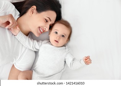 Portrait of mother with her cute baby lying on bed, top view. Space for text