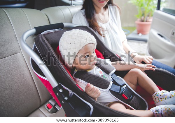 portrait of a Mother securing her baby in the car\
seat in her car