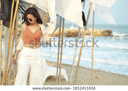 Portrait of motion blurred woman wearing sunglasses with blowing flags and blurred seascape in background. Picture was processed in soft vintage in purpose