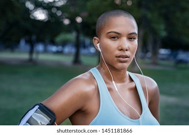 Portrait of motivated young woman resting after jogging. Beautiful focused bald girl take a break after run. Determined runner listening to music while jogging and looking at camera. - Powered by Shutterstock