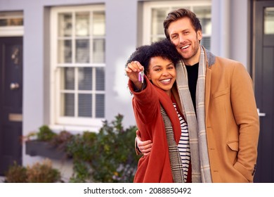 Portrait Of Multi Cultural Couple Outdoors On Moving Day Holding Keys To New Home In Fall Or Winter