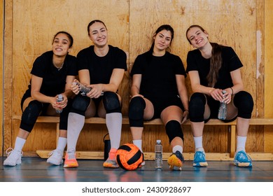 Portrait of a multicultural female teenage volleyball team sitting on court and smiling at the camera. A young sportswomen sitting on volleyball court on break and posing while smiling at the camera. - Powered by Shutterstock