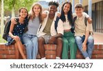 Portrait Of Multi-Cultural Secondary Or High School Students Sitting On Wall Outdoors At School