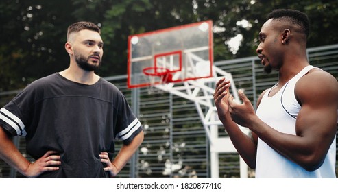 Portrait of multi-ethnic diverse male professional basketball players standing on outdoor court and talking. Handsome African American and Caucasian boys chatting about game. Streetball. Sport concept - Powered by Shutterstock