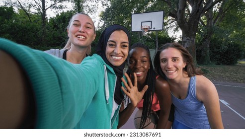 Portrait of Multiethnic Female Friends in Sports Clothes Posing for a Selfie Using a Smartphone. Group of Young Women Celebrating a Win in Outdoor Basketball Court by Taking a Photo for Social Media - Powered by Shutterstock