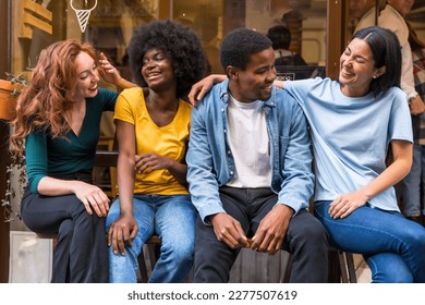 Portrait of multi-ethnic friends in a coffee shop sitting in the doorway of the shop window, embracing having fun - Shutterstock ID 2277507619