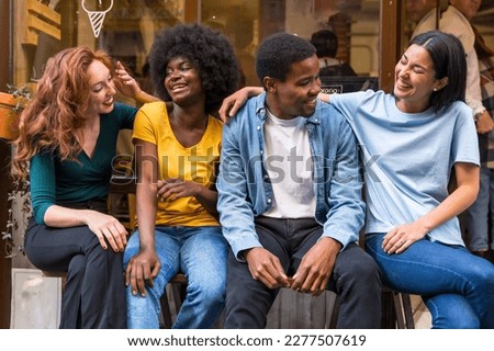 Portrait of multi-ethnic friends in a coffee shop sitting in the doorway of the shop window, embracing having fun
