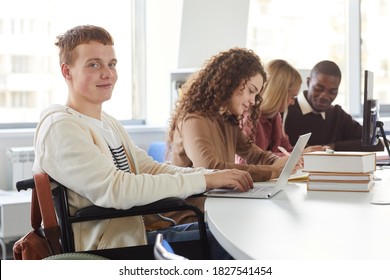 Portrait of multi-ethnic group of students using laptops while studying in college, featuring cheerful boy using wheelchair looking at camera - Powered by Shutterstock