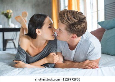 portrait of multiracial couple kissing each other while lying on bed together in bedroom