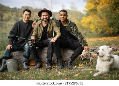 Portrait Of Multiracial Male Friends Sitting Together In Nature. Men After Fishing On River Or Lake Coast. Concept Of Leisure And Weekend In Nature. Idea Of Friendship And Spending Time Together
