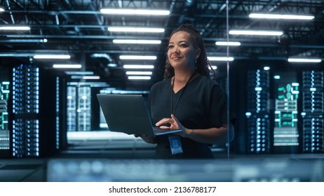 Portrait of Multiracial Mature Female IT Specialist Using Laptop, Standing in Data Center. Infrastructure Architect Works on Web Services. Cloud Computing, Server Analytics, Cyber Security Maintenance