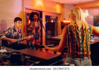 Portrait of a multiracial music band recording new album in a studio with their producer and sound engineer. Hispanic woman singing while caucasian man and woman are playing guitars. Copy space. - Powered by Shutterstock