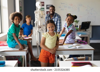 Portrait Of Multiracial Students And African American Young Male Teacher With Skeleton In Class. Unaltered, Education, Childhood, Teaching, Science, Stem And School Concept.